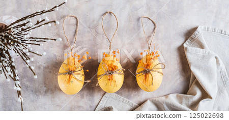 Three painted eggs with dried flowers for decoration on a gray background top view web banner 125022698