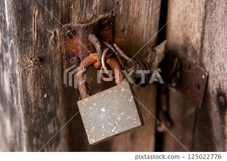 Old and rusty door lock hanging on the wooden door 125022776