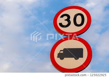 Traffic signs showing speed limit of 30 kilometers per hour and truck restriction against cloudy blue sky background 125022925