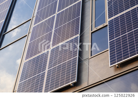 Solar panels installed on modern building facade reflecting sunlight on glass windows during bright clear day 125022926