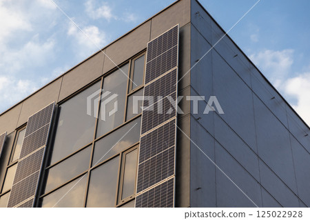 Solar panels on corner of modern glass building with clean architectural lines and evening light reflections Solar panels on corner of modern glass building with clean architectural lines and evening light reflections 125022928