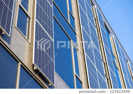 Vertical view of solar panels on modern office building generating renewable energy on sunny day with blue sky and glass reflections in urban architecture Vertical view of solar panels on modern office building generating renewable energy on sunny day with blue sky and glass reflections in urban architecture 125022949