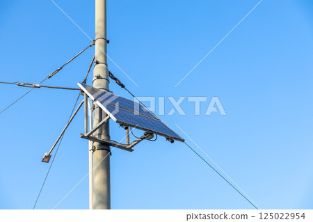 Modern solar panel attached to metal street pole with electric cables against clear blue sky, sustainable energy solution for smart city infrastructure Modern solar panel attached to metal street pole with electric cables against clear blue sky, sustainable energy solution for smart city infrastructure 125022954