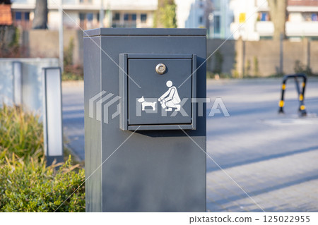 Public pet waste bin with dog cleanup symbol on urban street encouraging responsible pet ownership and clean environment awareness Public pet waste bin with dog cleanup symbol on urban street encouraging responsible pet ownership and clean environment awareness 125022955
