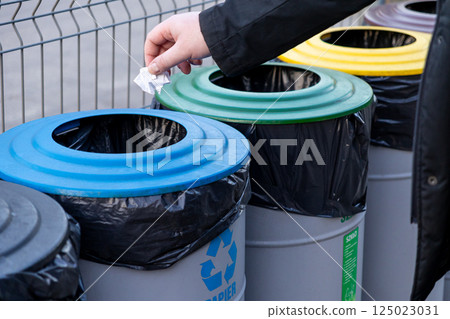 recycling paper into blue bin for eco waste segregation with colorful containers outdoors in public eco-friendly area 125023031