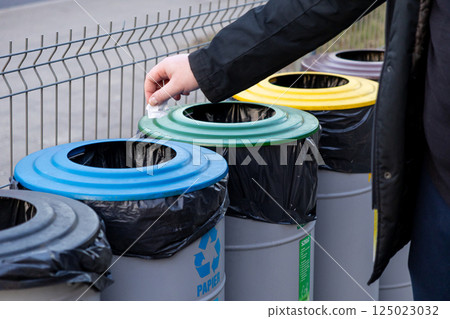 Man recycling trash into color-coded bins for paper, glass, plastic, and metal on city street, promoting waste separation and environmental awareness Man recycling trash into color-coded bins for paper, glass, plastic, and metal on city street, promoting waste separation and environmental awareness 125023032