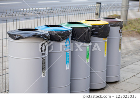 Row of colorful recycling bins for paper, plastic, metal, glass and mixed waste on city sidewalk, promoting organized waste separation and environmental awareness 125023033