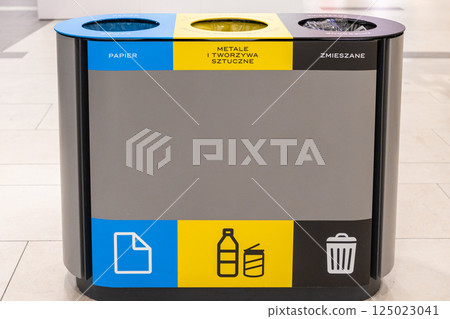 Modern indoor recycling bin with three colored compartments for paper, plastic, metal and general waste placed in public shopping mall environment 125023041