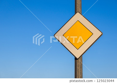 priority road traffic sign with yellow diamond shape on pole against clear blue sky symbolizing main road and traffic regulations on sunny day outdoors priority road traffic sign with yellow diamond shape on pole against clear blue sky symbolizing main road and traffic regulations on sunny day outdoors 125023044