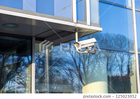 security surveillance camera on modern glass building corner with reflections of trees and sky in daytime light safety monitoring system urban architecture security surveillance camera on modern glass building corner with reflections of trees and sky in daytime light safety monitoring system urban architecture 125023052