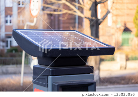 close up of solar panel on top of smart parking meter with blurred speed limit sign and residential architecture in background on sunny day in modern european city 125023056