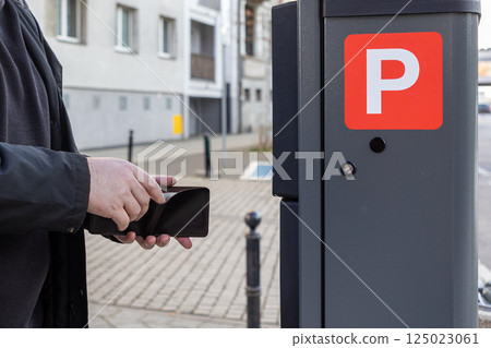 Man holding wallet in front of solar-powered parking meter in urban street setting, preparing for cash payment in city zone, close-up view of hands and machine Man holding wallet in front of solar-powered parking meter in urban street setting, preparing for cash payment in city zone, close-up view of hands and machine 125023061