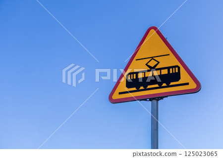 Warning road sign for approaching tramway crossing on a bright yellow triangle with red border against clear blue sky in urban transportation area 125023065