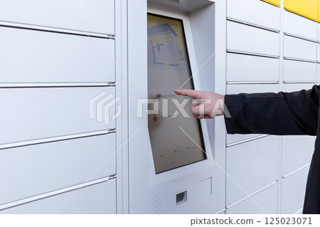 Man using touchscreen on white parcel locker terminal to collect or send package via modern contactless delivery system on urban street Man using touchscreen on white parcel locker terminal to collect or send package via modern contactless delivery system on urban street 125023071