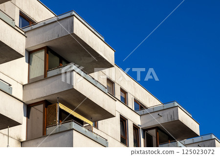 Modern residential apartment building with concrete balconies and glass railings under clear blue sky on a sunny day in contemporary urban neighborhood 125023072