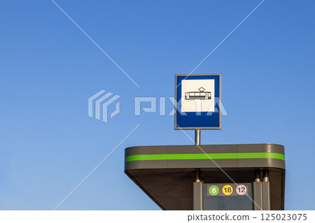 Tram stop sign on top of modern shelter against clear blue sky with line numbers visible and no people around on sunny day in urban public transportation area 125023075