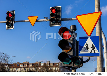 Traffic lights and road signs above crosswalk on urban street with blue sky background and pedestrian crossing symbol 125023078