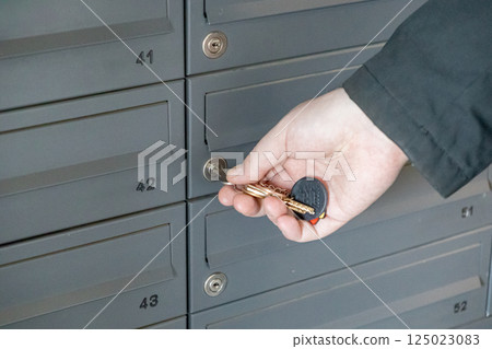 Hand with keys unlocking numbered mailbox in residential building lobby closeup view of keyhole and mail slots 125023083
