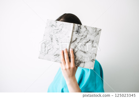 Woman holds a marble-covered notebook in front of her face against a white background. Creative self-expression and aesthetic stationery, journaling aesthetics, cozy notebooks, personal storytelling 125023345