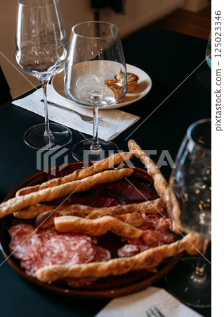 Plate of breadsticks and cured meats beside wine glasses and dessert during a tasting workshop. Wine workshop, food pairing, culinary education, table styling Plate of breadsticks and cured meats beside wine glasses and dessert during a tasting workshop. Wine workshop, food pairing, culinary education, table styling 125023346