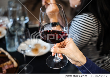 Close-up of a hand holding a glass of red wine during a casual social gathering Mindful consumption, wine tasting event, elevated at-home dining experiences 125023367
