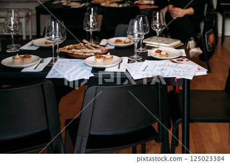 Empty chairs surround a wine workshop table with tasting cards, food samples, and glasses ready for participants. Wine workshop, pre-event setup, tasting preparation, hospitality training 125023384