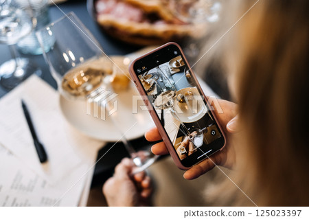 Person taking a photo of white wine during a food and wine tasting session. Highlights digital dining, visual storytelling, and aesthetic documentation Person taking a photo of white wine during a food and wine tasting session. Highlights digital dining, visual storytelling, and aesthetic documentation 125023397