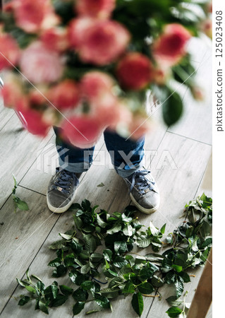 Florist standing over a floor scattered with green rose leaves after bouquet preparation. Revival of local floral businesses, shop small, ethical flowers, community-based commerce 125023408