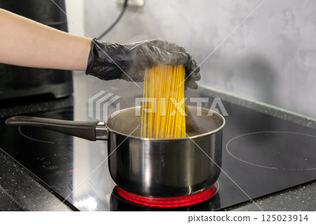The girl drops the pasta into the boiling water in the pot. Cooking pasta. Close-up The girl drops the pasta into the boiling water in the pot. Cooking pasta. Close-up 125023914