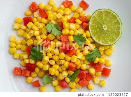 Fresh corn salad with vibrant red peppers and lime on a white plate 125025857