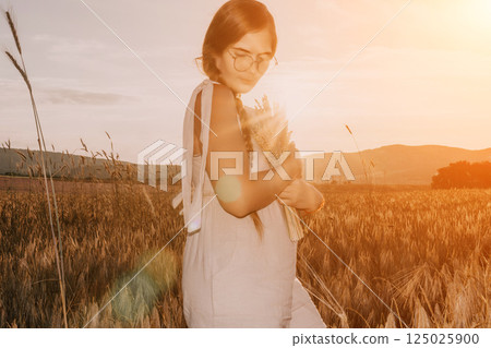 Woman wheat field. Agronomist, Woman farmer check golden ripe barley spikes in cultivated field. A woman is holding a bunch of wheat in her arms. 125025900
