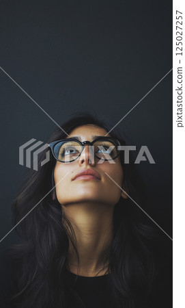 Thoughtful Woman Looking Up Against Dark Background 125027257