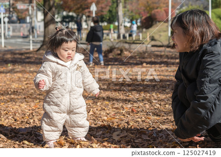 [一名 1 歲的孩子站在落葉覆蓋的冬季公園玩耍] 125027419