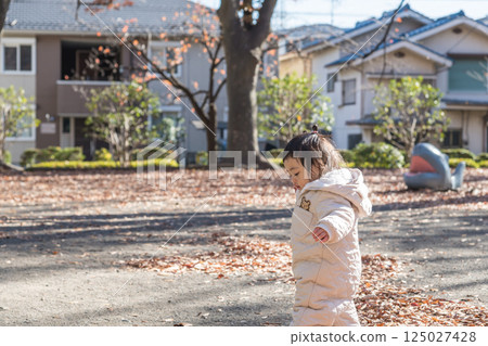 [A one-year-old child stands up, playing in a winter park covered with fallen leaves] 125027428
