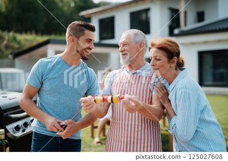 Parents and adult son preparing food for a family barbecue. 125027608