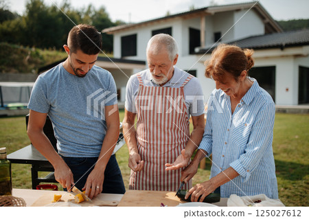 Parents and adult son preparing food for a family barbecue. Parents and adult son preparing food for a family barbecue. 125027612