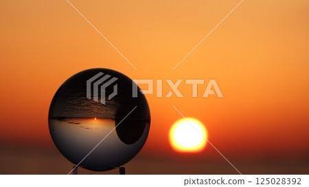 Glass ball and the sun setting over the sea 125028392