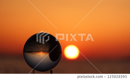 Glass ball and the sun setting over the sea Glass ball and the sun setting over the sea 125028393