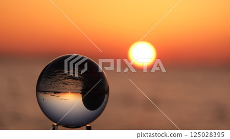 Glass ball and the sun setting over the sea Glass ball and the sun setting over the sea 125028395