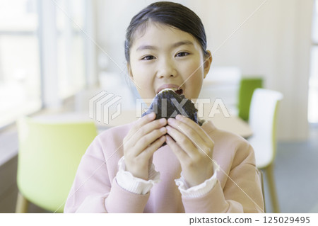 一名小學生在餐廳大口吃著飯糰。照片由東京電子專門學校、電波學園學校法人提供。 125029495