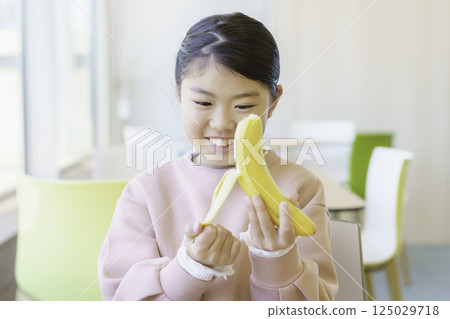 An elementary school girl eating a banana at a restaurant. Photo courtesy of Tokyo Electronics College, Denpa Gakuen School Corporation. 125029718