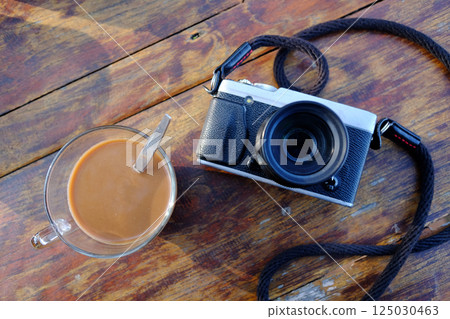 Vintage mirrorless camera and a glass cup of hot coffee on wooden table. Top view 125030463