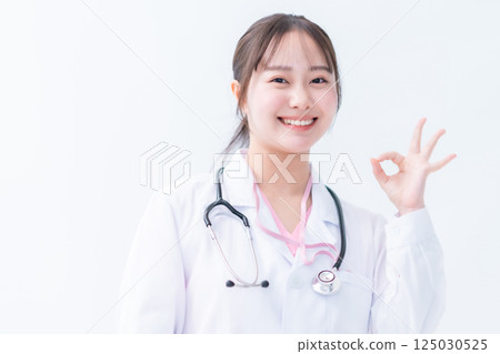 A trainee doctor in a white coat making an OK pose on a white background 125030525
