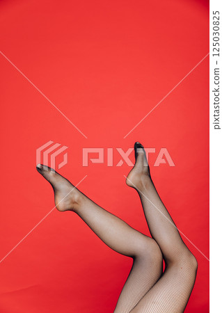 Slender female legs in black stockings, tights on a red background Slender female legs in black stockings, tights on a red background 125030825