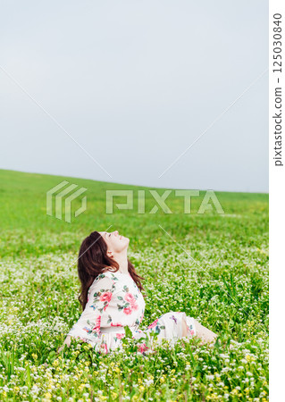 woman sitting in a field with flowers in spring and smiling 125030840