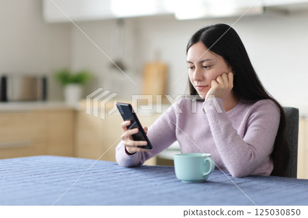 Asian woman using smart phone in a kitchen 125030850