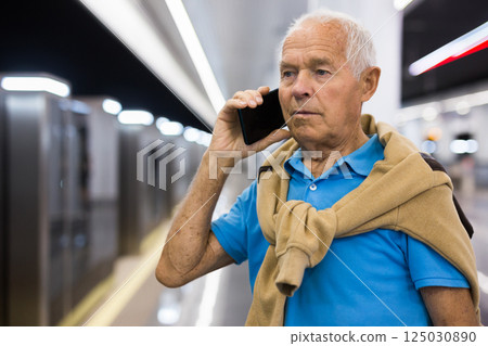 Portrait of man standing in underground station and talking on mobile phone 125030890