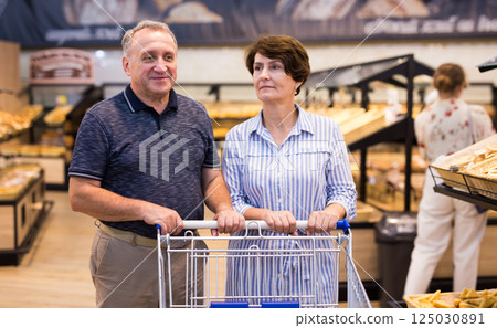 Elderly couple buys bread and baking in grocery section of supermarket 125030891