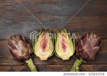 Half and whole purple raw roman artichokes on a dark wooden table top view. Fresh italian vegetables 125032338
