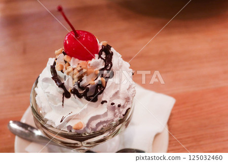 close up of Sundae cream ice cream with cherry on top and chocolate sauce with a tea spoon 125032460
